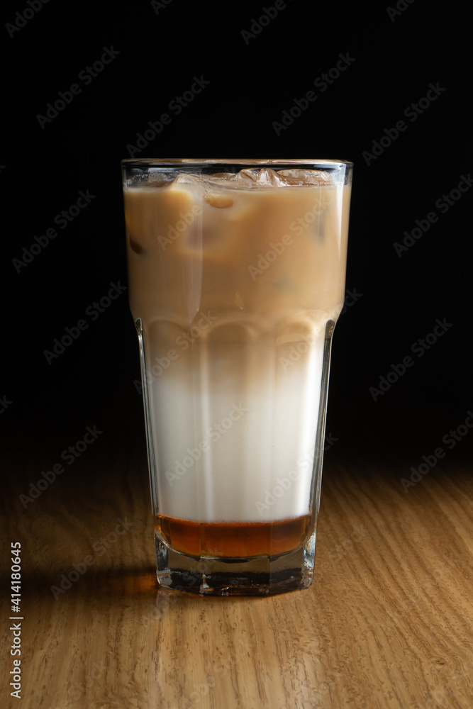 Ice latte macchiato coffee with syrup and ice in a transparent glass on a wooden table Ice latte macchiato coffee with syrup and ice in a transparent glass on a wooden table