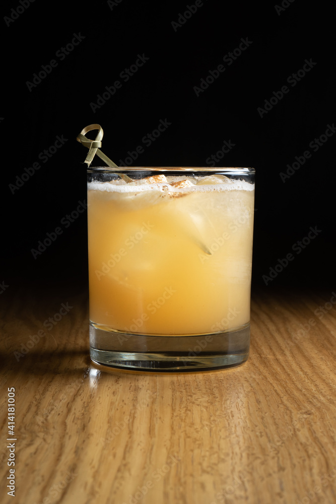 Penicillin - a whiskey-based alcoholic cocktail with lemon juice and honey-ginger syrup in a transparent glass on a wooden table Penicillin - a whiskey-based alcoholic cocktail with lemon juice and honey-ginger syrup in a transparent glass on a wooden table