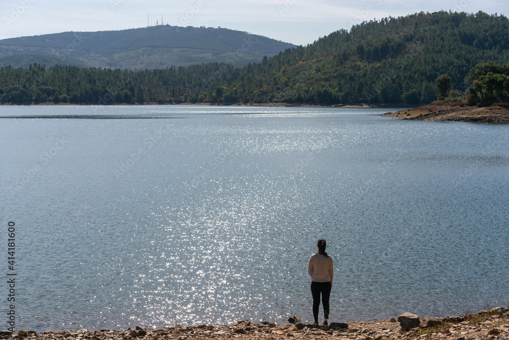 Caucasian girl looking at the lake water of Apartadura dam with mountains with trees landscape in Alentejo, Portugal Caucasian girl looking at the lake water of Apartadura dam with mountains with trees landscape in Alentejo, Portugal