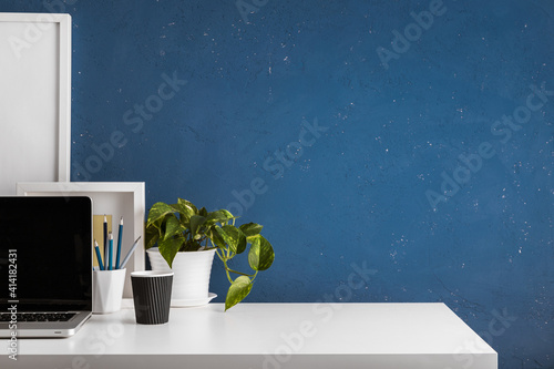 Home office desk with blue wall and white table mock up.	
