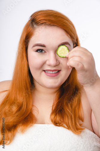 Vertical shot of a young ginger-haired woman with cucumber piece isolated over white background