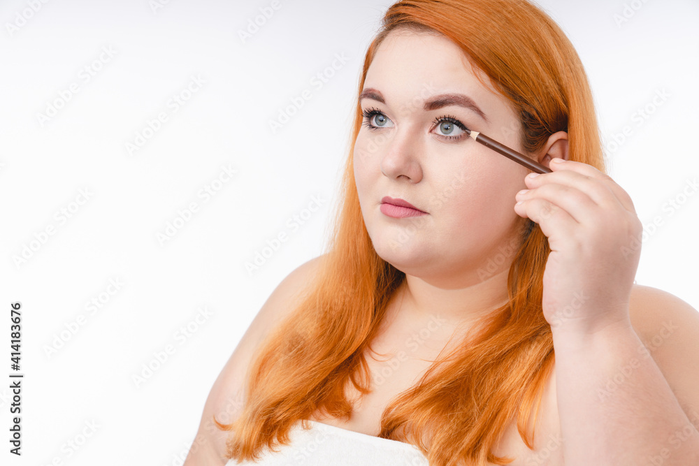 Corpulent redhead woman in spa towel using eye pencil isolated over white background Corpulent redhead woman in spa towel using eye pencil isolated over white background