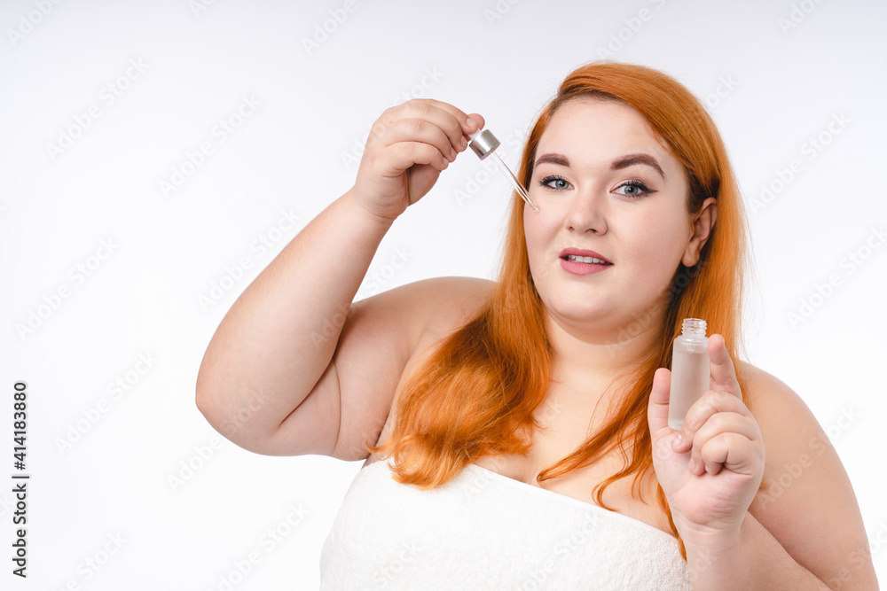 Young ginger-haired woman with beauty bottle in spa towel isolated over white background Young ginger-haired woman with beauty bottle in spa towel isolated over white background