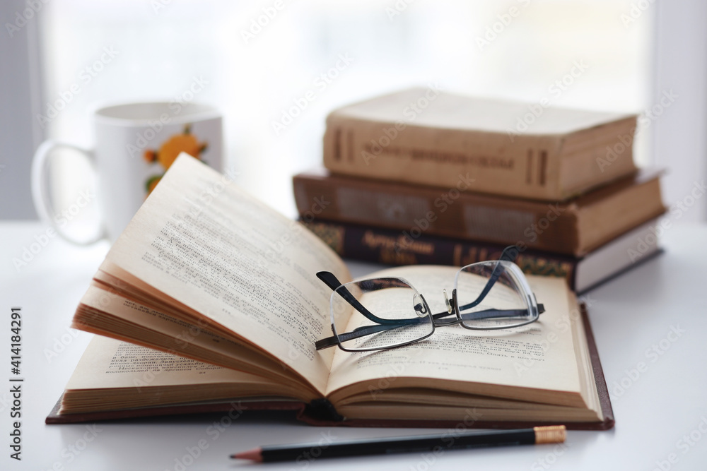 Old books, glasses, pencil and cup of coffee on white table background against window light with copy space Old books, glasses, pencil and cup of coffee on white table background against window light with copy space