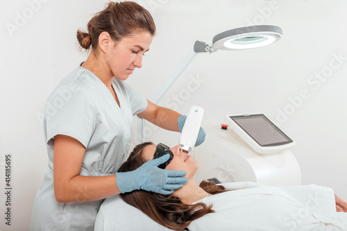 Partial view of young woman receiving laser hair removal epilation on face in salon. Young woman making body hair removal laser depilation. 