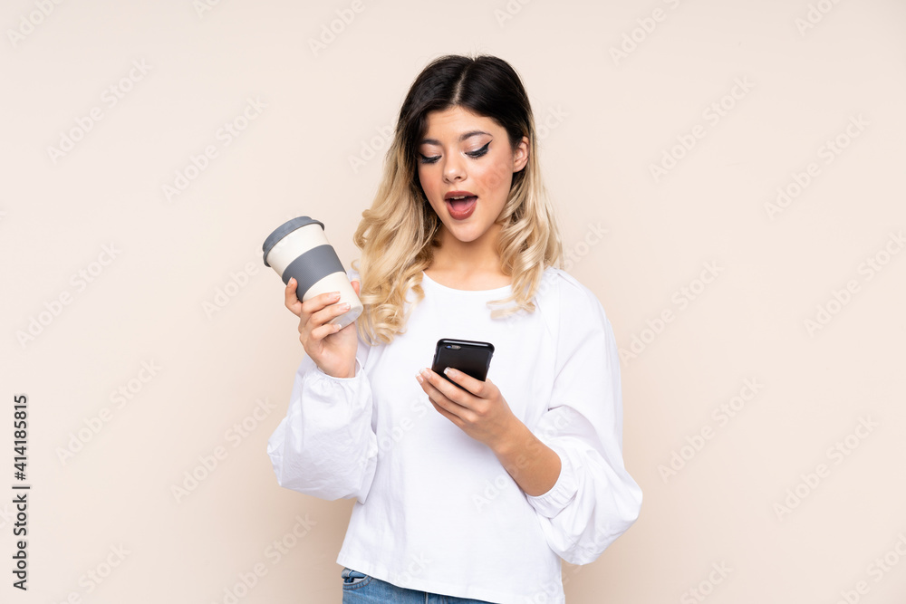 Teenager girl isolated on beige background holding coffee to take away and a mobile while thinking something Teenager girl isolated on beige background holding coffee to take away and a mobile while thinking something