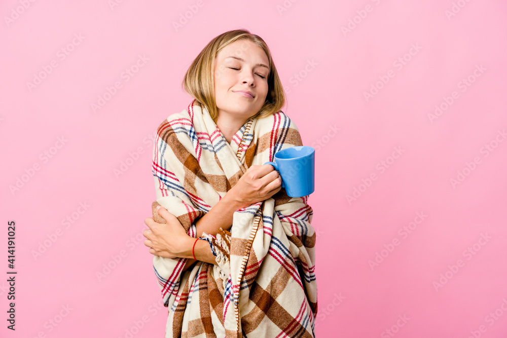 Young russian woman wrapped in a blanket drinking coffee hugs, smiling carefree and happy. Young russian woman wrapped in a blanket drinking coffee hugs, smiling carefree and happy.