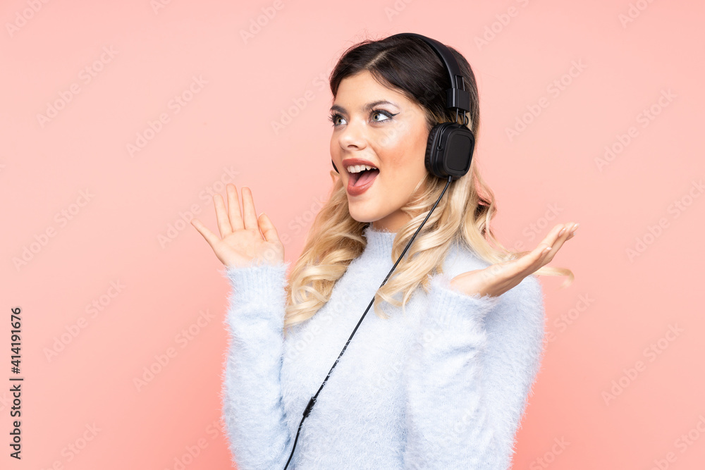 Teenager girl isolated on pink background surprised and listening music Teenager girl isolated on pink background surprised and listening music