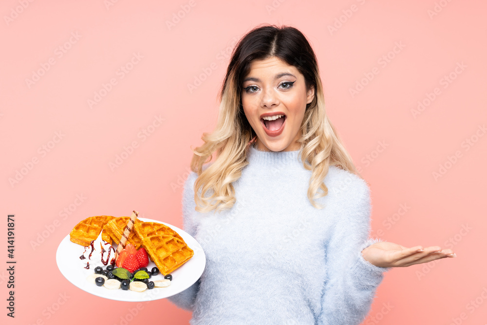 Teenager girl holding waffles on isolated pink background with shocked facial expression
