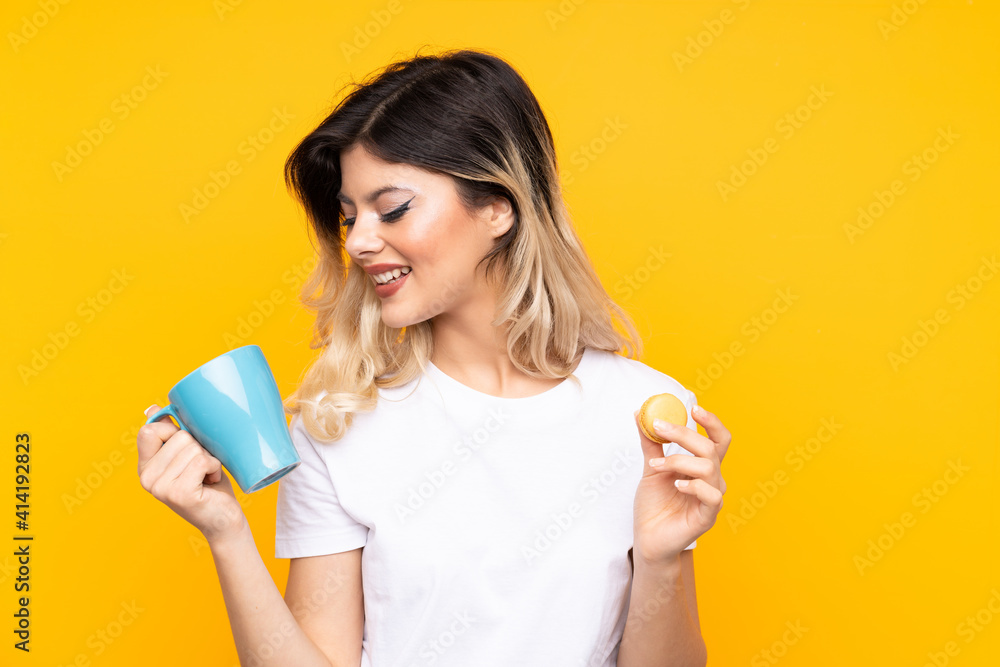 Teenager girl isolated on yellow background holding colorful French macarons and a cup of milk Teenager girl isolated on yellow background holding colorful French macarons and a cup of milk