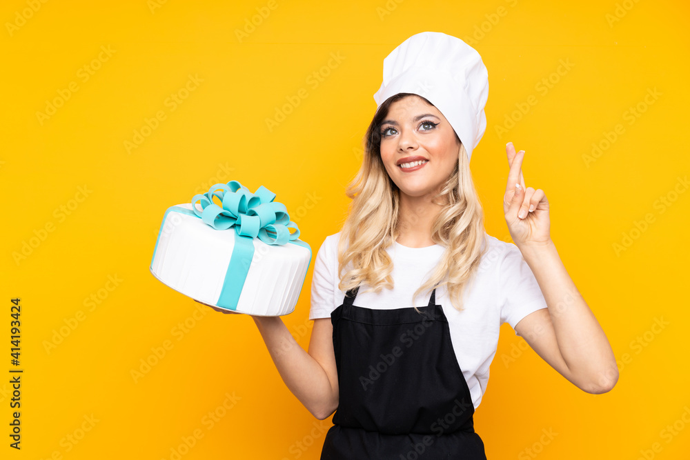 Teenager girl pastry holding a big cake isolated on yellow background with fingers crossing Teenager girl pastry holding a big cake isolated on yellow background with fingers crossing