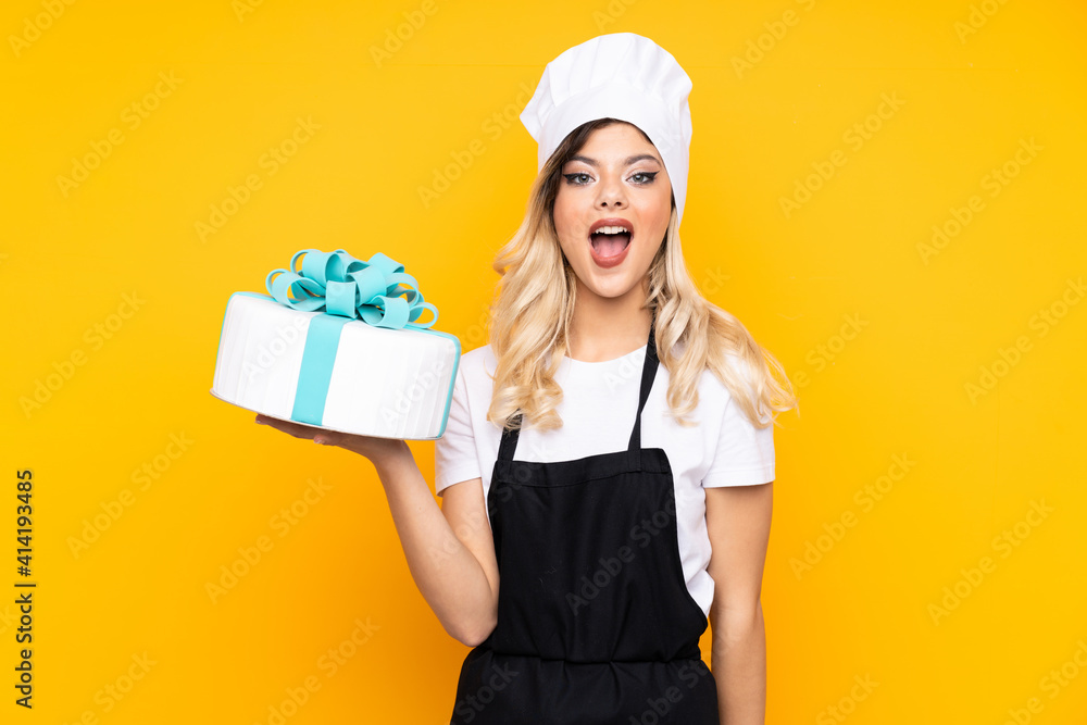 Teenager girl pastry holding a big cake isolated on yellow background with surprise facial expression Teenager girl pastry holding a big cake isolated on yellow background with surprise facial expression