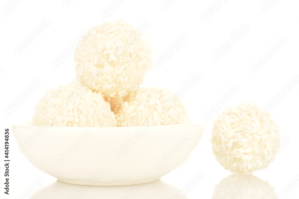 Several round sweets with coconut flakes in a ceramic white plate, close-up, isolated on white.