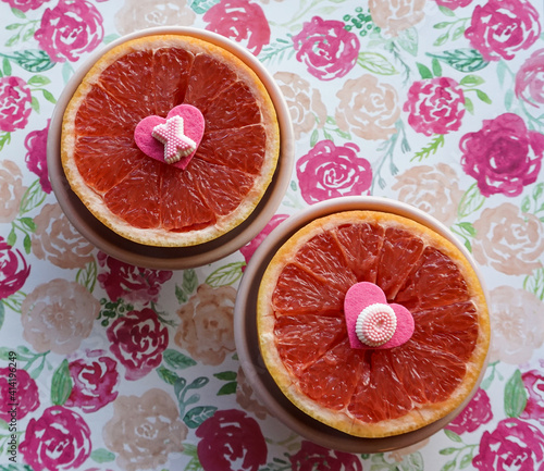 Pink grapefruit halves with heart and candy decorations, colorful floral background.