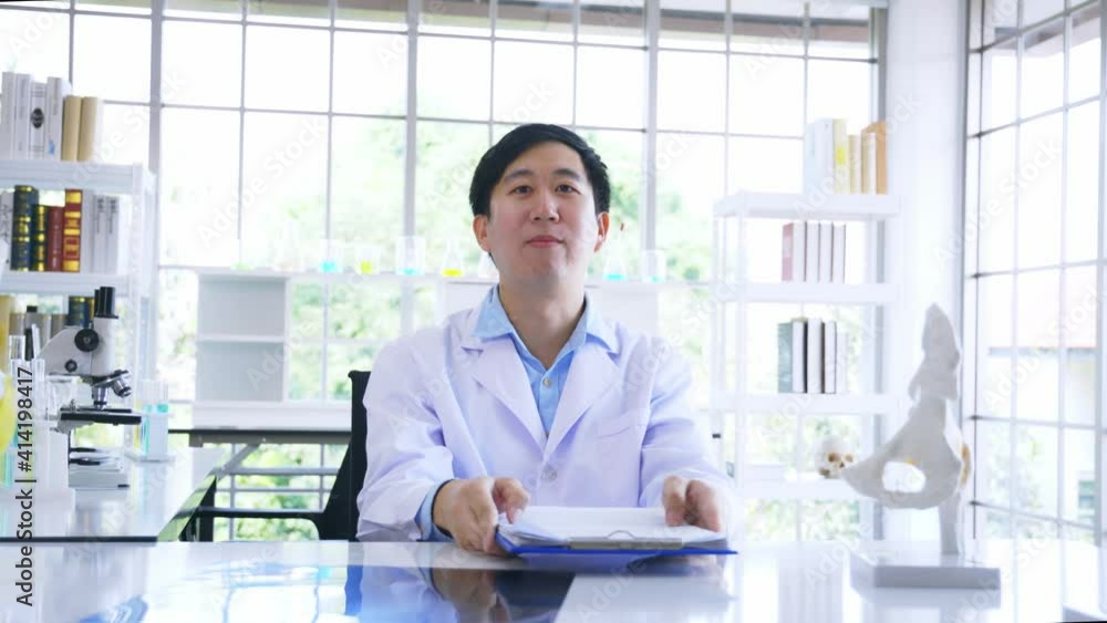 Asian male doctor sitting in hospital cabin reading and analysing issue in lungs of patient with x-ray film while wearing a labcoat. High quality 4k footage Asian male doctor sitting in hospital cabin reading and analysing issue in lungs of patient with x-ray film while wearing a labcoat. High quality 4k footage