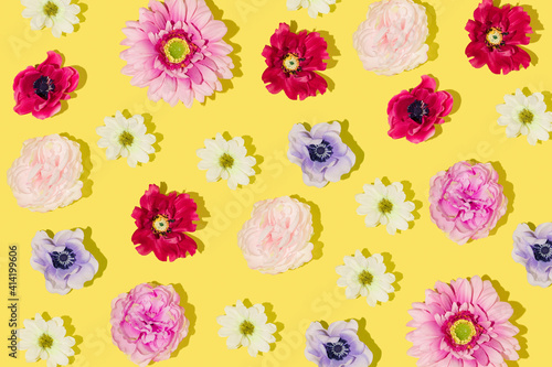 Creative pattern made with yellow, orange, rose, raspberry red, pink, purple and dark blue flowers on bright yellow background. Minimal flat lay. Creative arrangement with bloom. Spring aesthetic