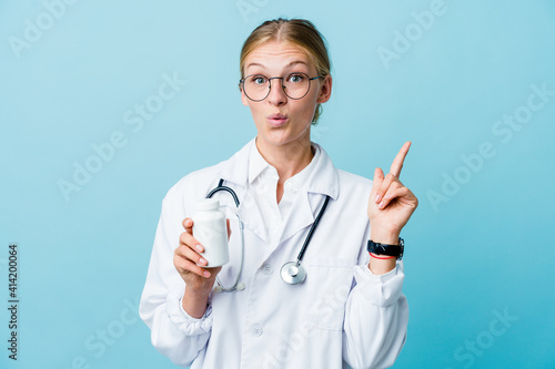Young russian doctor woman holding pills bottle on blue having some great idea  concept of creativity.