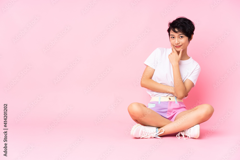 Young Vietnamese woman with short hair sitting on the floor over isolated pink background smiling Young Vietnamese woman with short hair sitting on the floor over isolated pink background smiling