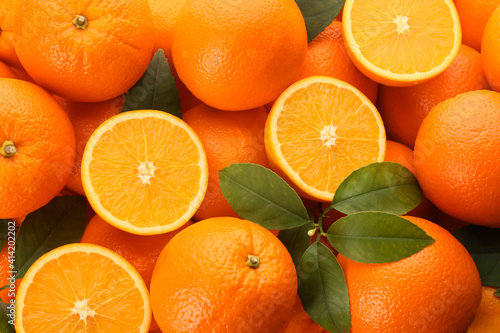 Cut and whole fresh ripe oranges with green leaves as background, top view