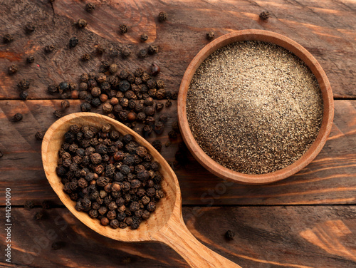 Black peppercorns in a spoon and black ground pepper in a plate on a wooden background. Top view photo