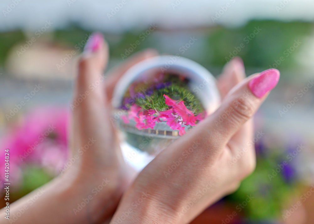 Girl holds a glass ball in her hands. Beautiful reflection of flowers in the refractive sphere