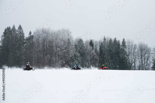 Tree drivers are driving snowmobiles on snow field in winter and forest background.
