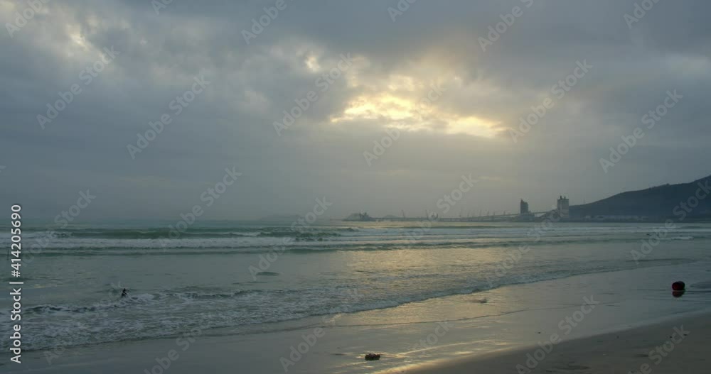 A large sun appears from behind the clouds, and large mountains touch the horizon and coast. Asian beach background. The trail of the sun on the waves in the sand. A large sun appears from behind the clouds, and large mountains touch the horizon and coast. Asian beach background. The trail of the sun on the waves in the sand.
