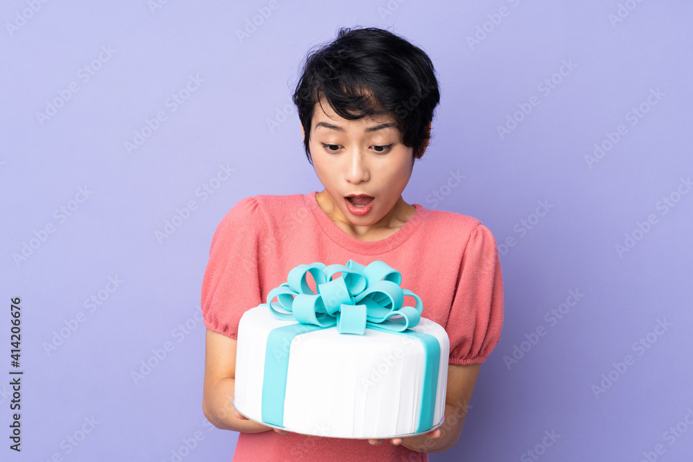 Young Vietnamese woman with short hair holding a big cake over isolated purple background Young Vietnamese woman with short hair holding a big cake over isolated purple background