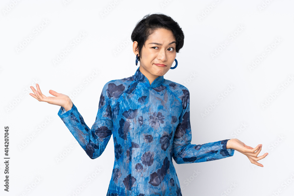Young Vietnamese woman with short hair wearing a traditional dress over isolated white background having doubts while raising hands Young Vietnamese woman with short hair wearing a traditional dress over isolated white background having doubts while raising hands