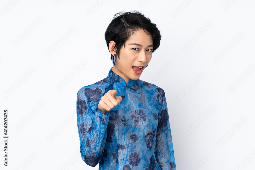 Young Vietnamese woman with short hair wearing a traditional dress over isolated white background surprised and pointing front Young Vietnamese woman with short hair wearing a traditional dress over isolated white background surprised and pointing front