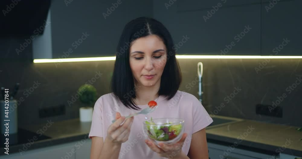 Gorgeous happy smiling young woman eating freshly prepared vegetable salad from bowl in contemporary kitchen,front view Gorgeous happy smiling young woman eating freshly prepared vegetable salad from bowl in contemporary kitchen,front view