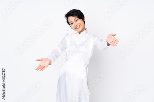 Young Vietnamese woman with short hair wearing a traditional dress over isolated white background presenting and inviting to come with hand