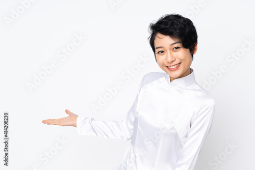 Young Vietnamese woman with short hair wearing a traditional dress over isolated white background extending hands to the side for inviting to come
