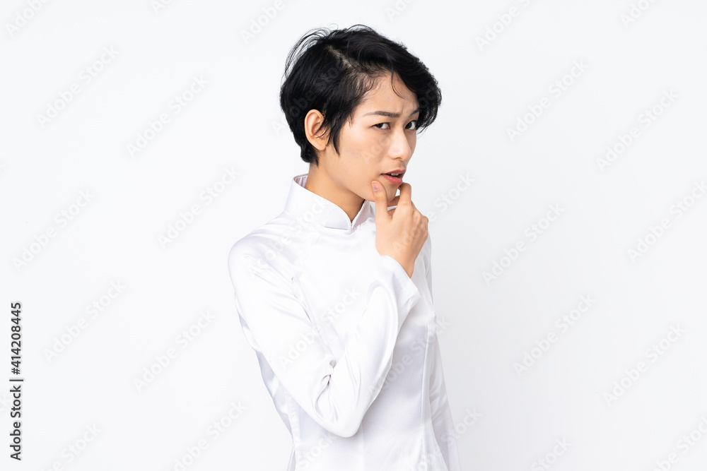Young Vietnamese woman with short hair wearing a traditional dress over isolated white background having doubts Young Vietnamese woman with short hair wearing a traditional dress over isolated white background having doubts
