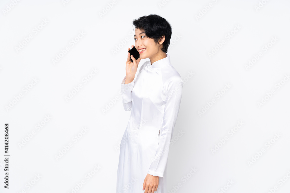 Young Vietnamese woman with short hair wearing a traditional dress over isolated white background keeping a conversation with the mobile phone with someone Young Vietnamese woman with short hair wearing a traditional dress over isolated white background keeping a conversation with the mobile phone with someone