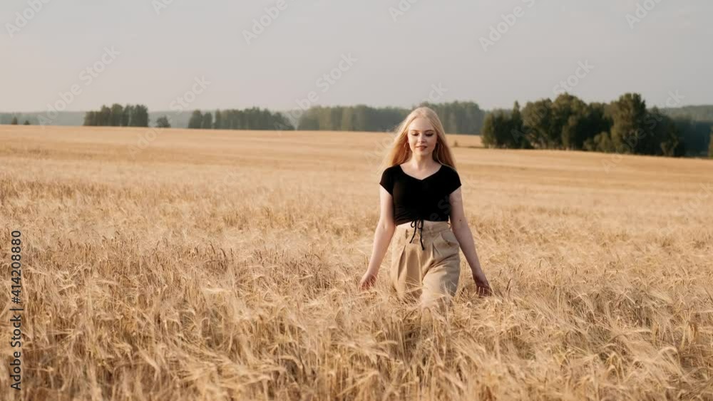 Joyful young girl enjoying nature and warm sunlight outdoors. Happy blondy woman walking and smiling in wheat field during sunny summer day. Healthy natural organic lifestyle. Joyful young girl enjoying nature and warm sunlight outdoors. Happy blondy woman walking and smiling in wheat field during sunny summer day. Healthy natural organic lifestyle.