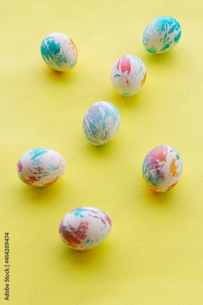 seven abstractly colored Easter eggs lie on a bright yellow background