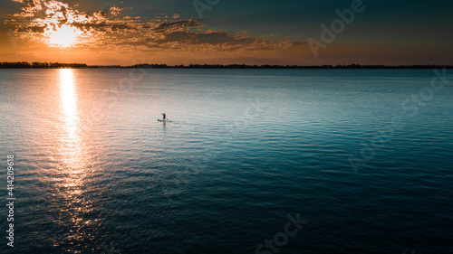 Vista Aérea de una persona sobre un Bote o Kayac, Stand Up Paddle sobre el mar, lago junto a un hermoso atardecer