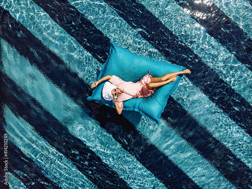 Top view of a slim cute charming woman in a bathrobe and with a towel on her head and sunglasses, floating in a pool on an inflatable mattress. Overflowing water. Relaxation concept