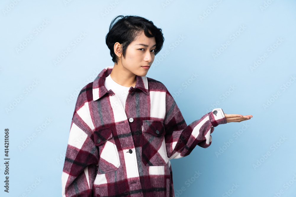 Young Vietnamese woman with short hair over isolated background holding copyspace with doubts