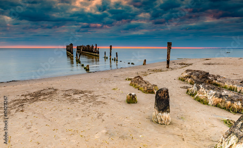Old broken fishing pier at sandy beach of the Baltic Sea at sunset, concept o...