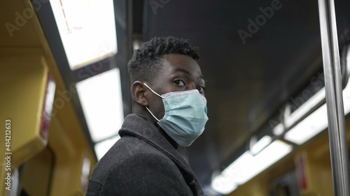 African man standing in subway metro wearing coronavirus mask underground commute