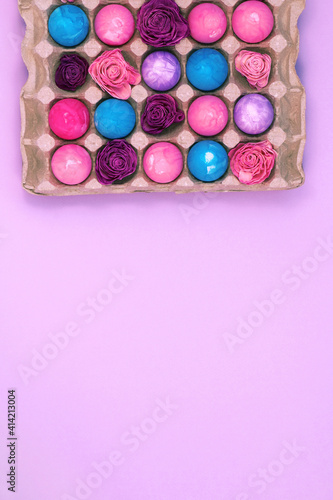 Easter eggs painted with gouache and dried flowers in egg box on violet pink background, copy space, vertical image