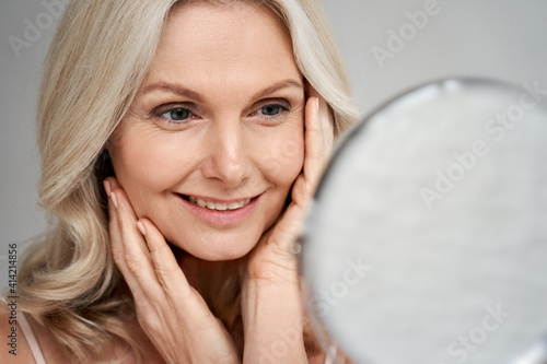 Fotografia Happy 50s middle aged woman model touching face skin looking in mirror