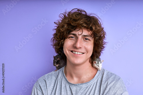 smiling man with two small rats near face on shoulders, concept of friendship between man and animal. isolated purple background