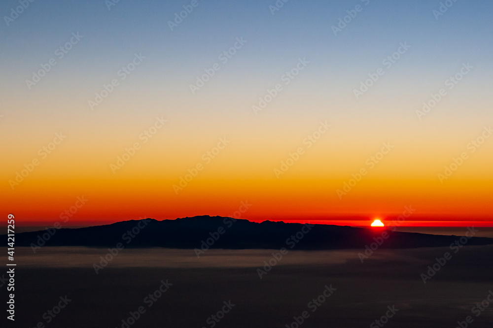 Sunrise red sun behind Canary Island La Gomera in sea. View from Pico del Teide mountain in El Teide National park. Tenerife, Canary Islands, Spain