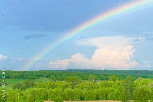 Summer landscape with colorful rainbows, green forest and rural field