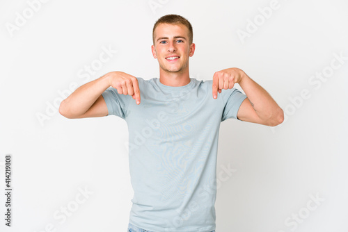 Young caucasian handsome man points down with fingers, positive feeling.