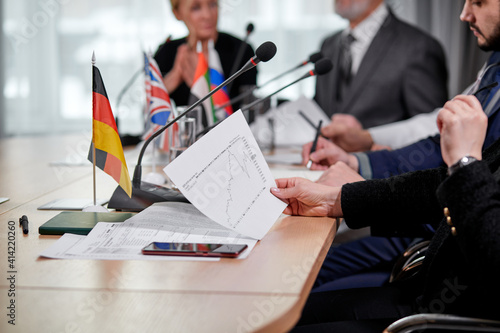 close-up photo of chart document in hands of female executive during interracial business meeting in modern office, people sitting at desk photo