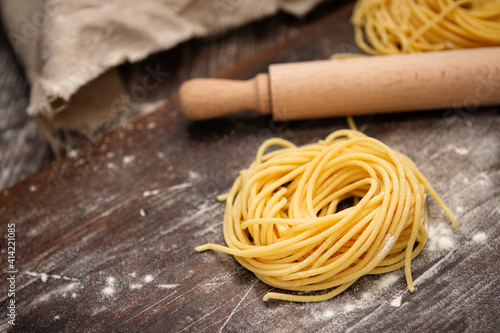 Uncooked fresh spaghetti nests on a wooden table with a rolling pin. Italian pasta homemade